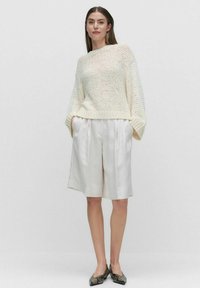 Witte gebreide trui met een losse pasvorm, lange mouwen en geribde onderrand, gecombineerd met crèmekleurige geplooide shorts. Gelaagd, lichtgewicht materiaal.