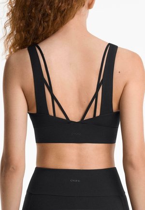 Black sports bra with wide straps, featuring a layered back design with multiple thin straps. Made from a smooth, stretchy fabric.