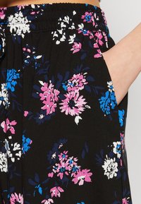 Telas negras con estampado floral colorido en rosa, blanco y azul. Presenta una cintura elástica y un detalle de bolsillo lateral.