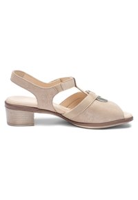Beige Wildleder-Sandalette mit niedrigem Absatz, offenem Zehenbereich, Slingback-Riemen, elastischem Seitendetail und metallischer runder Verzierung am vorderen Riemen.