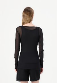 Černý top s dlouhým rukávem, hladký a přiléhavý na těle, s průhlednými rukávy. Má kulatý výstřih a vrstvený lem, doplněný černými šortkami.