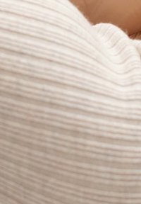 Mjuk, strukturerad tyg i ljus beige med subtila horisontella ränder, som bildar en böjd form och visar en slät, taktil yta.