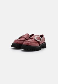 Mocassins en cuir verni rouge avec une épaisse semelle noire, ornés d'une boucle décorative embellie de cristaux et de détails de couture prononcés.