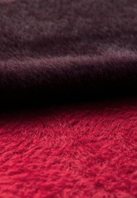 Dos trozos de tela expuestos: un material morado oscuro y esponjoso en la parte superior y una tela roja brillante y texturizada debajo, ambos con un aspecto suave.
