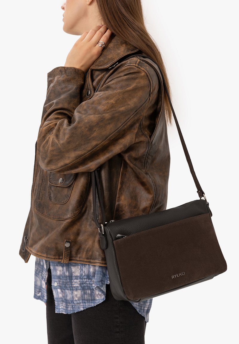 Personne portant une veste en cuir marron et une chemise à carreaux bleue, avec un sac bandoulière RYŁKO marron foncé et noir sur l'épaule.