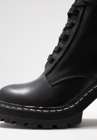 Svart läderankelboot med rund tå, utrustad med en tjock sula, framträdande spår och kontrasterande vit söm längs kanten.