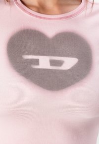 Ribbed pink tank top with a light gray heart pattern featuring a stylized logo at the center. The neckline has pink stitching accents.