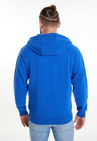 Sweat-shirt à capuche bleu avec une texture lisse, des poignets et une taille côtelés. Il dispose d'une poche kangourou et d'une capuche avec cordon.