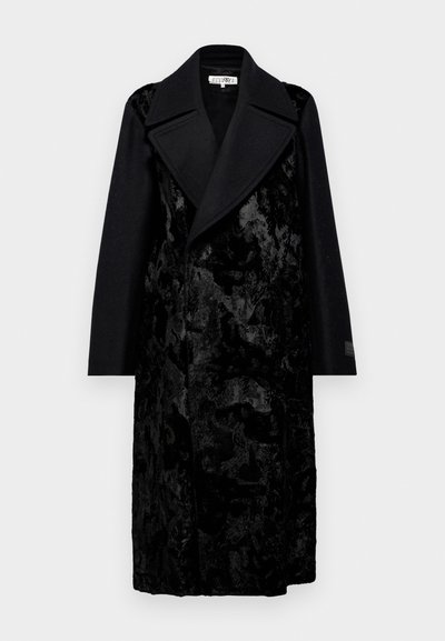 Long black coat featuring a textured fabric with a velvet-like finish, wide lapels, and straight sleeves. Simple design with no visible fasteners.