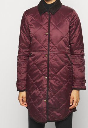 Długa bordowa pikowana kurtka z czarnym sztruksowym kołnierzem, zapięciem na zatrzaski i kieszeniami bocznymi, na osobie stojącej nieruchomo.