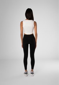 Valkoinen lyhyt toppi yhdistettynä mustiin korkeavyötäröisiin leggings-housuihin ja valkoisiin tennareihin, joissa on mustia yksityiskohtia, nähtynä takaa.