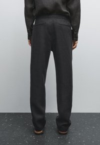 Donkergrijze linnenbroek met een relaxte pasvorm, elastische tailleband, twee achterzakken en subtiele textuur, gedragen met een bijpassend shirt.