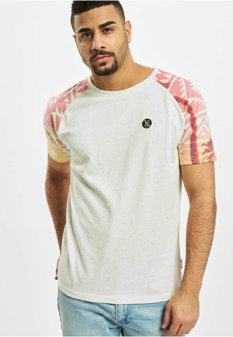 Hvit prikkete t-skjorte med mønstrede rosa og oransje raglan-sleeves. Har en rund svart logo på venstre bryst.