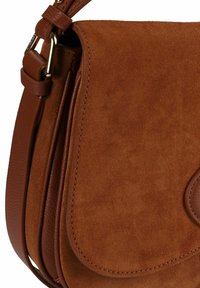 Bruine suède schoudertas met een glad leren band, voorzien van een afgeronde klep en contrasterende stikseldetails, met een zachte textuur.