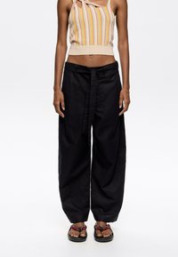 Black wide-leg trousers with a tied belt, made of a lightweight fabric. Worn with a striped cropped top and beaded sandals.