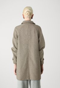 Grijze jas van een wolmix met een rugpas, oversized mouwen en knoopmanchetten. Heeft een rechte snit en een gestructureerde stof.