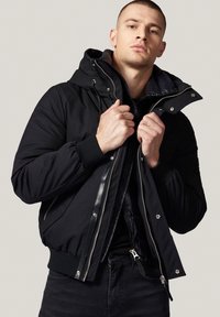 Czarna kurtka puchowa z odpinanym kapturem, zamkiem błyskawicznym, ściągaczami na mankietach oraz miękką podszewką. Posiada elegancki krój i jednolity kolor.