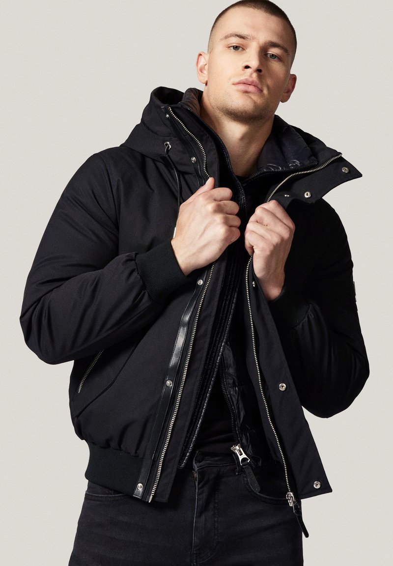 Czarna kurtka puchowa z odpinanym kapturem, zamkiem błyskawicznym, ściągaczami na mankietach oraz miękką podszewką. Posiada elegancki krój i jednolity kolor.