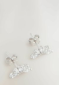 Hopeiset nappikorvakorut, joissa on kolme pientä päärynänmuotoista kirkasta jalokiveä, aseteltuna riviin jokaisessa korviksessa.