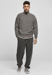 Suéter gris de cuello alto con un tejido texturizado, sobre una camisa gris clara, combinado con pantalones oscuros gris sueltos y zapatillas grises.