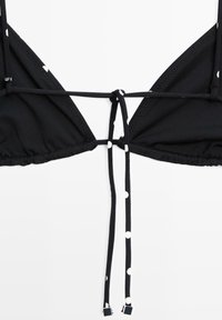 Haut de bikini triangle noir à pois blancs avec de longues attaches pendantes, posé à plat sur une surface blanche.