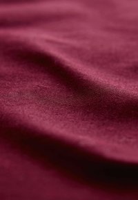 Burgunderfarbener Stoff mit glatter Textur, der sanfte Falten und einen subtilen Glanz zeigt und dabei seine reiche Farbe und Webdetails betont.
