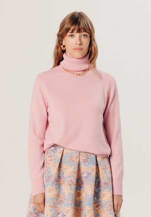 Rosa Rollkragenpullover aus weichem Material, kombiniert mit einem gemusterten Rock mit floralen Designs in Pastellfarben. Lässige, taillierte Silhouette.