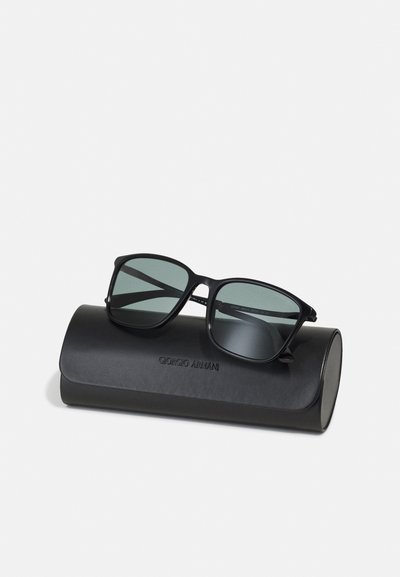 Sorte solbriller med rektangulære rammer og grønne linser, som hviler på et svart lærdeksel preget med "Giorgio Armani."