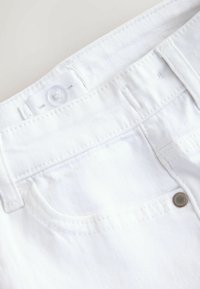 Hvide denimshorts med frontlukning med knap, syninger og en lille metalnitte på lommen for forstærkning.