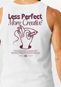 White sleeveless shirt featuring maroon text and graphic of a hand holding a pencil, with the phrase "Less Perfect More Creative" prominently displayed.