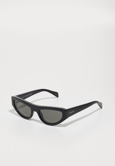 Black, cat-eye sunglasses with dark lenses. Made of smooth plastic, featuring a minimalist design. Embossed brand logo on the temple.