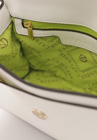 Interno di una borsa a tracolla in pelle bianca con una fodera in tessuto verde, dotato di una tasca con zip e di un motivo ripetuto con il logo "CAFÉ NOIR".