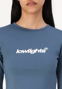 Langermet topp i slate blue bomullsblanding med rund hals og brodert "lowlights"-logo i hvitt over brystet.