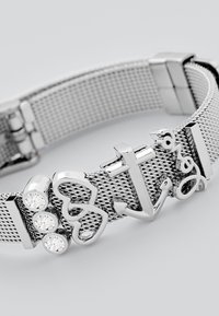 Bracciale in mesh argentato con ciondoli a forma di cuore e di ancora, accentuato da tre piccoli cristalli rotondi su un lato.