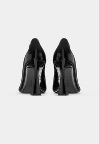 Cizme cu toc înalt din piele patent neagră, cu vârf ascuțit și tocuți unghiulari unici, având o textură netedă și un design minimalist.
