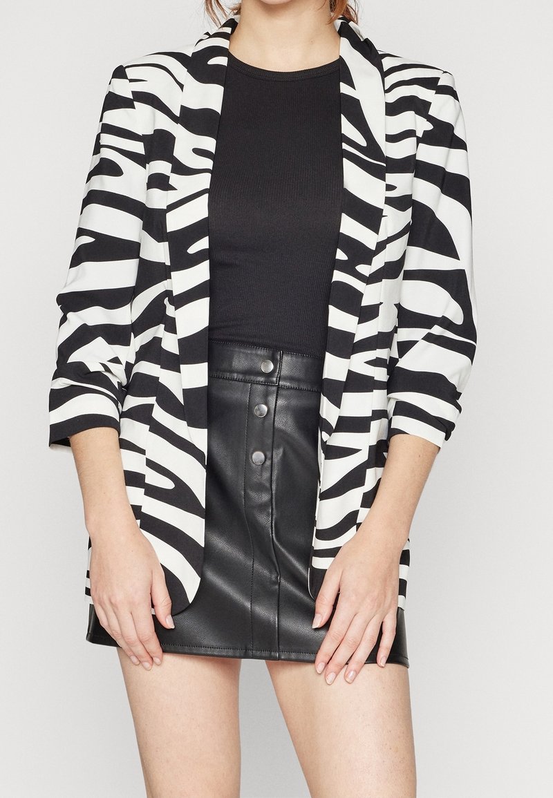 Blazer s černobílými pruhy zebry a tříčtvrtečními rukávy, doplněný o přiléhavý černý top a mini sukně z černé umělé kůže.