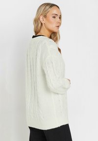 Cardigan bianco in maglia con design a trecce, polsini e orlo a costine. Vestibilità ampia con scollo rotondo e tessuto texturizzato.