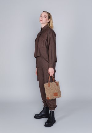Giacca cropped marrone con due tasche a toppa, pantaloni tapered abbinati, stivali neri stringati e una borsa marrone chiaro testurizzata con dettagli in pelle.