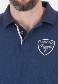 Polo shirt navy avec une patte de boutonnage à deux boutons, col contrastant et badge brodé arborant "Ruckfield French Rugby Club."