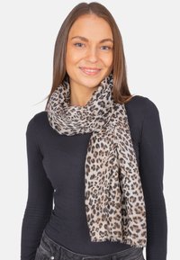 Foulard en imprimé léopard dans des tons beiges et bruns, fabriqué en tissu léger, avec des bords effilochés et une texture douce, enroulé autour du cou du mannequin.