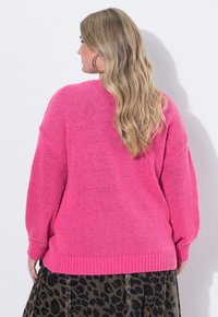 Rosa stickad tröja med lös passform och ribbad fåll, tillsammans med en kjol i svart och brunt leopardmönster. Tröjan har sänkta axlar och strukturmaterial.