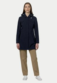 Veste imperméable marine avec capuche, manches longues et fermeture à boutons. Caractéristiques d'un logo sur la poitrine et d'une coupe ajustée mi-longue.