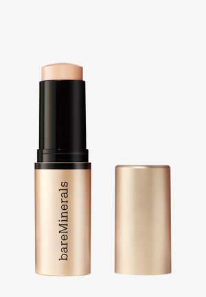 Fond de teint BareMinerals en stick avec produit de maquillage beige étendu à partir d'un tube doré et noir, capuchon retiré et placé à côté.
