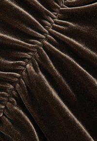 Bruine fluwelen stof met een zachte textuur, met doorgestikte plooien overal. Het oppervlak lijkt glad en behaaglijk.