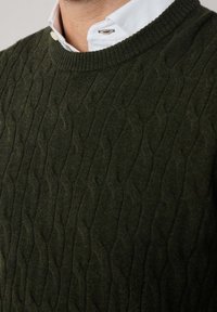 Maglione a coste verde scuro con scollatura rotonda, motivo testurizzato e polsini a costine, indossato sopra una camicia bianca con colletto.