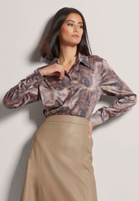 Lange mouwen, overhemd met paisleypatroon in glanzende stof, met een klassieke kraag en knoopdetails, gecombineerd met een high-waisted beige leren rok.