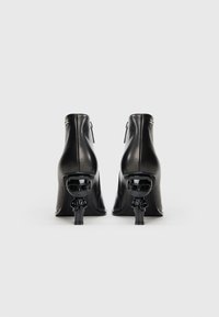 Black leather ankle boots with a glossy finish, featuring a sculpted, novelty heel design of a figure in sunglasses, metallic accents, and zippers.