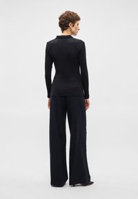 Top preto canelado de mangas longas emparelhado com calças largas listradas em azul-marinho, apresentando uma silhueta ajustada e textura suave.