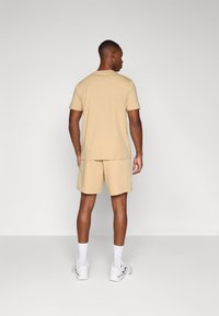 Conjunto de T-shirt e calções de algodão bege, design liso com mangas curtas e cintura elástica, combinado com ténis brancos e meias.