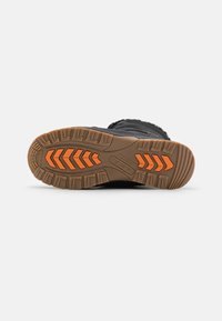 Suela de bota de invierno negra con surcos profundos para tracción, que presenta una base de goma marrón y acentos naranjas en un patrón de zigzag.